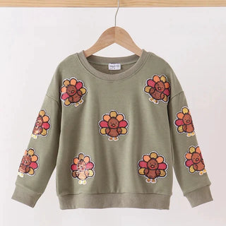An olive green crewneck sweatshirt with a cartoon turkey pattern, hanging on a wooden hanger against a plain white wall.