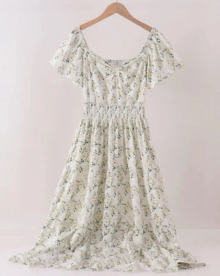 A short-sleeve off-the-shoulder maxi dress with a delicate green and blue floral print on a cream background, hanging on a wooden hanger against a plain light wall.