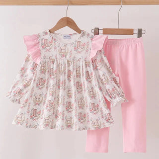 A two-piece girls' outfit set hanging on wooden hangers against a plain light background. The set includes a long-sleeve smocked blouse with pink ruffle sleeves and a pink and beige bunny print, paired with solid light pink pants.