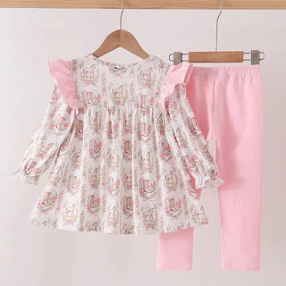 A toddler girl's two-piece clothing set hanging on wooden hangers against a plain light background. The set includes a long-sleeve smocked blouse with pink ruffle sleeves and a white floral print, paired with solid light pink leggings.