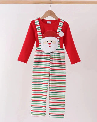 A children's holiday-themed two-piece outfit hanging on a wooden hanger against a plain light background. The set includes a solid red long-sleeve top and matching red-and-green striped overalls with a white Santa face applique on the chest.