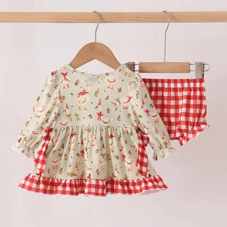 A toddler girl's two-piece outfit hanging on wooden hangers against a plain light background. The set includes a long-sleeve cream-colored dress with a red, orange, and yellow print, and matching red-and-white gingham check bloomers.