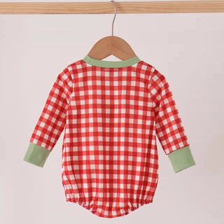 A baby long-sleeve romper with a red and white gingham check pattern and sage green trim on the collar and cuffs, hanging on a wooden hanger against a light beige background.