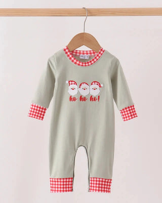 A baby long-sleeve footless romper in sage green, featuring red and white gingham trim at the collar, cuffs, and hem, with a graphic of three Santa Claus faces and the text 'ho ho ho!' on the chest. The romper is displayed on a wooden hanger hanging from a wooden rod against a light beige background.