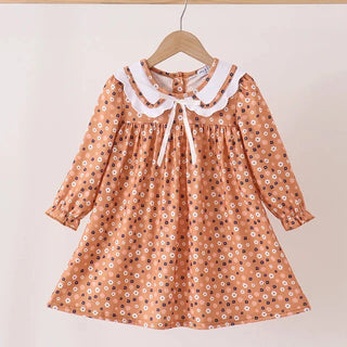 A toddler girl's long-sleeve dress in a warm terracotta orange color, decorated with a small white and black floral pattern. It features a white ruffled Peter Pan collar with a white tie at the neckline, hanging on a wooden hanger against a plain light beige background.