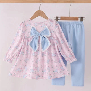 A toddler girl's two-piece outfit hanging on wooden hangers against a light pink background. The set includes a long-sleeve pink gingham top with a light blue bow at the back neckline and a matching light blue pair of pants.