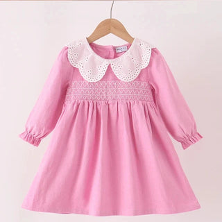 A pink long-sleeve girls dress with a white eyelet Peter Pan collar and smocked bodice, hanging on a wooden hanger against a plain light background.