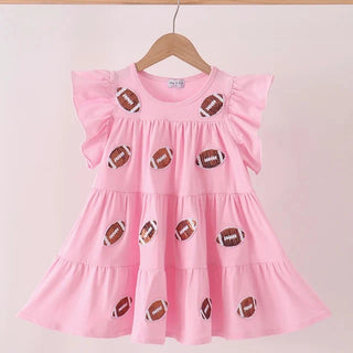 A pink tiered girls dress with ruffled sleeves, decorated with embroidered football motifs, hanging on a wooden hanger against a light pink background.