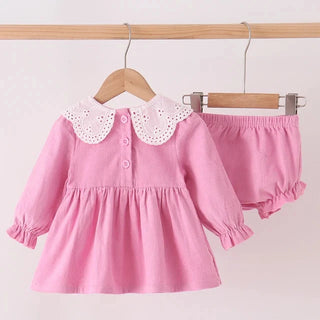 A pink toddler girl's two-piece outfit set consisting of a long-sleeve dress with a white eyelet Peter Pan collar and matching pink ruffled bloomers, hanging on wooden hangers against a plain light background.