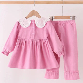 A two-piece baby girl's outfit set consisting of a pink long-sleeve dress with a white eyelet Peter Pan collar and matching pink pants, hanging on wooden hangers against a plain white background.
