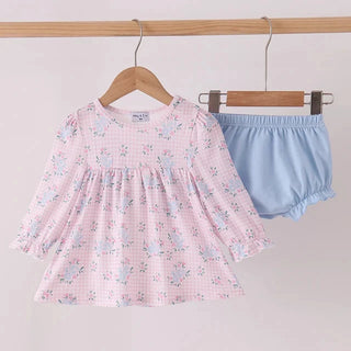 A baby girl's two-piece outfit hanging on wooden hangers against a plain light background. The set includes a long-sleeve smocked blouse in light pink with a white gingham pattern and small blue floral details, paired with light blue ruffled bloomers.