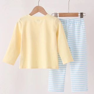 A children's two-piece pants set hanging on wooden hangers from a wooden rod. The set includes a pale yellow long-sleeve top and light blue and white striped pants.
