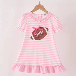 A pink and white striped short-sleeve dress with a ruffled neckline and hem, featuring a football applique with a pink bow on the chest, hanging on a wooden hanger.
