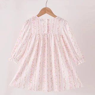 A long-sleeve dress with a delicate pink and green floral print on a white base, hanging on a wooden hanger from a light wood rod against a plain off-white background.