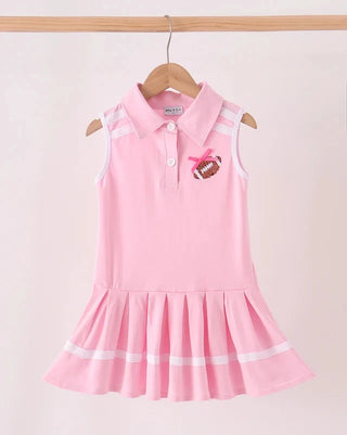 A pink sleeveless girls' dress with a polo collar, white shoulder stripes, and a pleated skirt, hanging on a wooden hanger against a light pink background.