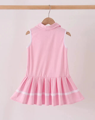 A pink sleeveless dress with a mock neck and pleated ruffled skirt, hanging on a wooden hanger against a light pink background.