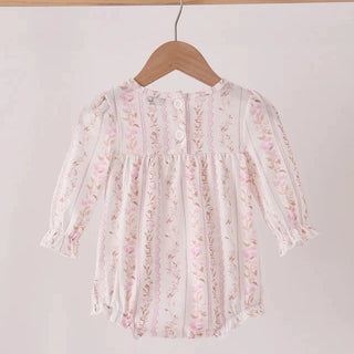 A long-sleeve baby top with a delicate pink and green floral print on a white base, hanging on a wooden hanger from a wooden clothing rack against a plain light background.