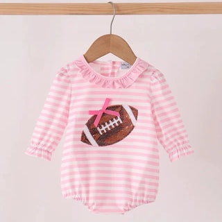 A baby long-sleeve romper with pink and white horizontal stripes, featuring a ruffled neckline and a football graphic on the chest with a pink bow, hanging on a wooden hanger.
