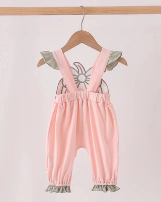 A baby romper in light pink with ruffled sage green shoulder and leg accents, hanging on a wooden hanger against a plain light background.