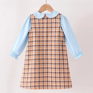 A children's dress hanging on a wooden hanger against a plain light background. The dress has a brown and beige plaid body with a light blue collar and light blue long sleeves with ruffled cuffs.