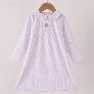 A light pink long-sleeve baby dress with a white polka dot pattern, featuring a Peter Pan collar and a small embroidered turkey on the chest, hanging on a wooden hanger.