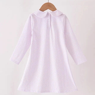 A light pink long-sleeve dress with a small white polka dot pattern, hanging on a wooden hanger from a wooden clothes rack against a plain off-white background.