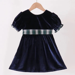 A navy blue velvet toddler dress with short puff sleeves and a green and white plaid waistband, hanging on a wooden hanger against a plain white background.