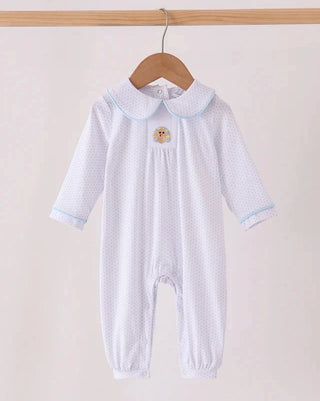 A baby long-sleeve footless romper in white with tiny polka dots, featuring a light blue Peter Pan collar and cuffs, and a small embroidered turkey on the chest. The romper is hanging on a wooden hanger from a wooden clothes rack against a plain light beige background.