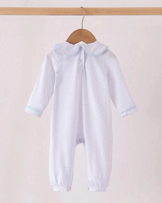 A white long-sleeve baby romper with a tiny polka dot pattern, featuring a light blue trim around the Peter Pan collar and cuffs, hanging on a wooden hanger against a light beige background.