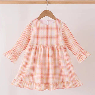 A toddler girl's long-sleeve dress with a white, orange, and light pink gingham plaid pattern, hanging on a wooden hanger from a light wood clothing rack against a plain off-white wall.