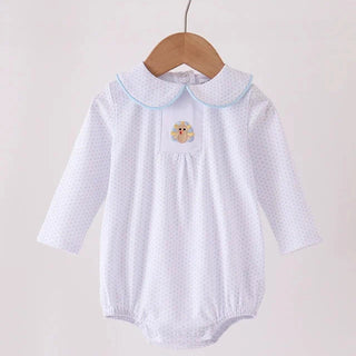 A white long-sleeve baby romper with a tiny polka dot pattern, featuring a light blue Peter Pan collar and a small embroidered turkey  patch on the chest, hanging on a wooden hanger.