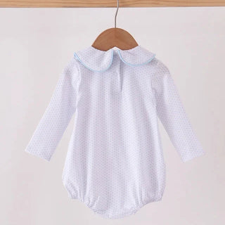 A white long-sleeve baby romper with a tiny polka dot pattern and a light blue Peter Pan collar, hanging on a wooden hanger from a wooden clothes rack.