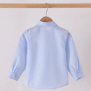 A light blue long-sleeve button-up shirt hanging on a wooden hanger from a wooden clothes rack, shown from the back against a plain off-white background.