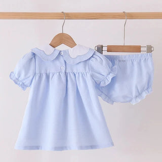 A baby girl's two-piece outfit set consisting of a light blue short-sleeve dress with a white Peter Pan collar and matching light blue ruffled bloomers, hanging on wooden hangers from a wooden rod against a plain off-white background.