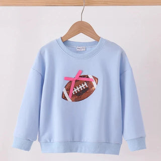 A light blue crewneck sweatshirt hanging on a wooden hanger, featuring a graphic of a brown football with a pink ribbon tied to it on the front.