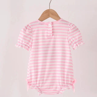 A pink and white striped short-sleeve baby romper with ruffled trim, hanging on a wooden hanger from a light wood clothes rack against a plain off-white background.