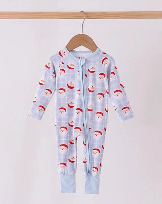 A baby long-sleeve footless zip-up sleeper hanging on a wooden hanger from a wooden rod. The sleeper has a light blue and white plaid pattern with a repeating print of Santa Claus' faces wearing red hats.
