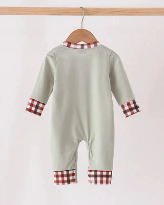 A baby long-sleeve footless romper in a light sage green, hanging on a wooden hanger from a wooden clothes rack. The romper features brown and white gingham plaid trim at the collar, cuffs, and hem.