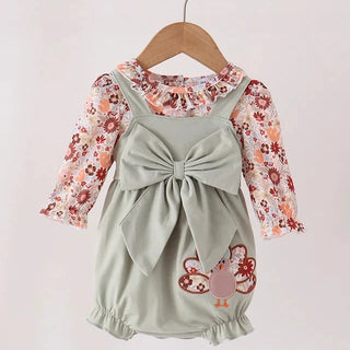 A toddler girl's two-piece outfit hanging on a wooden hanger against a plain light background. The set includes a sage green romper with a large front bow and a butterfly applique, layered over a long-sleeve floral shirt in pink, red, and white.