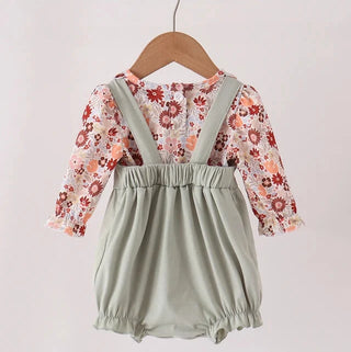 A toddler girl's two-piece outfit hanging on a wooden hanger. The set includes sage green bubble shorts with shoulder straps over a long-sleeve floral top with a ruffled collar and cuffs.