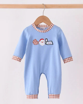 A baby's light blue one-piece jumpsuit with red and white gingham trim on the collar, cuffs, and hems, featuring a festive Christmas-themed graphic on the chest. The jumpsuit is displayed on a wooden hanger hanging from a wooden rod against a plain off-white background.