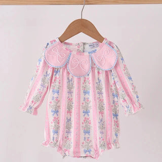 A pink long-sleeve baby bubble with a floral print and three large embroidered bow details on the collar, hanging on a wooden hanger against a light background.
