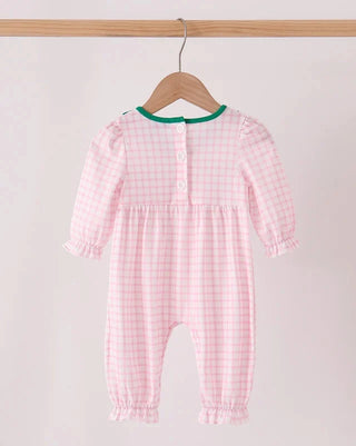 A baby long-sleeve romper in a pink and white gingham check pattern, hanging on a wooden hanger from a wooden clothes rack. The romper features a green trim along the neckline and button closures down the front.