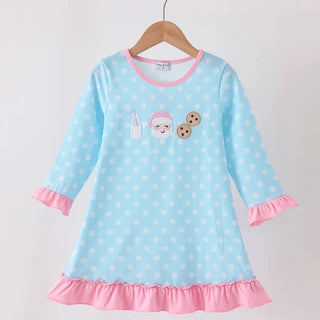 A light blue long-sleeve girl dress with white polka dots, pink ruffled trim at the cuffs and hem, and a cute cartoon character printed on the chest, hanging on a wooden hanger against a white wall.