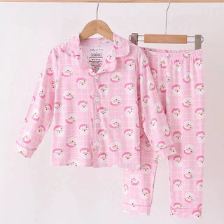 A two-piece children's pajama set hanging on wooden hangers against a plain white background. The set includes a long-sleeve button-front top and matching pants, both in light pink with a repeating rainbow and sun face print.