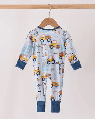 A baby long-sleeve footless one-piece pajama hanging on a wooden hanger, featuring a light blue background with a construction vehicle print in yellow, orange, and dark blue.
