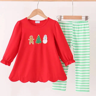 A two-piece children's outfit hanging on a wooden hanger bar, featuring a bright red long-sleeve top with a scalloped hem and holiday graphics, paired with mint green and white striped pants.