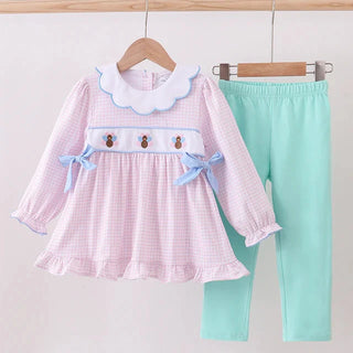 Children's outfit with pink checkered dress and mint green pants on a wooden hanger against a white background.