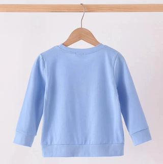 A light blue long-sleeve crewneck sweatshirt hanging on a wooden hanger from a wooden clothes rack, shown from the back against a plain off-white background.