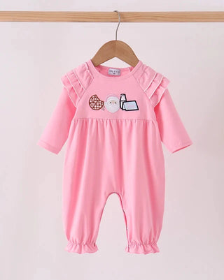 A pink baby long-sleeve romper with ruffled shoulder details and a cute cartoon patchwork design on the chest, hanging on a wooden hanger against a light pink background.